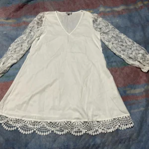 Chi Chi London women’s white dress in size L/XL laid flat, featuring long sheer lace sleeves, a V-neckline, and a decorative crochet lace hem.