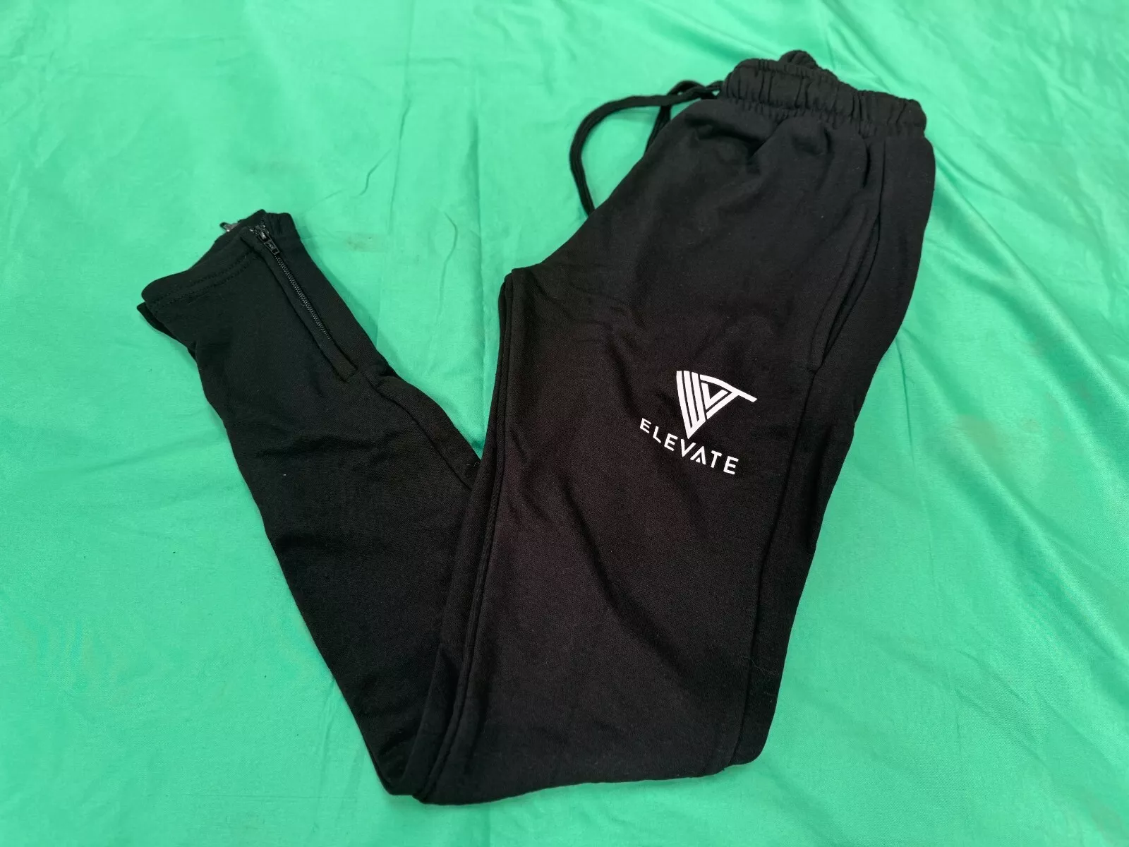 Unfolded black Elevate joggers with white logo and zip cuff design